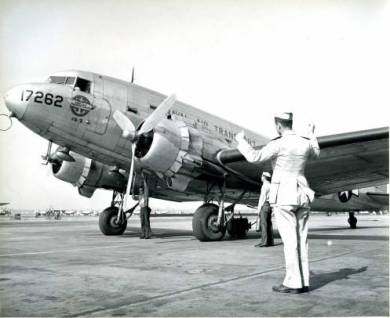 A man in uniform stands before a Naval Air Transport plane, circa 1945